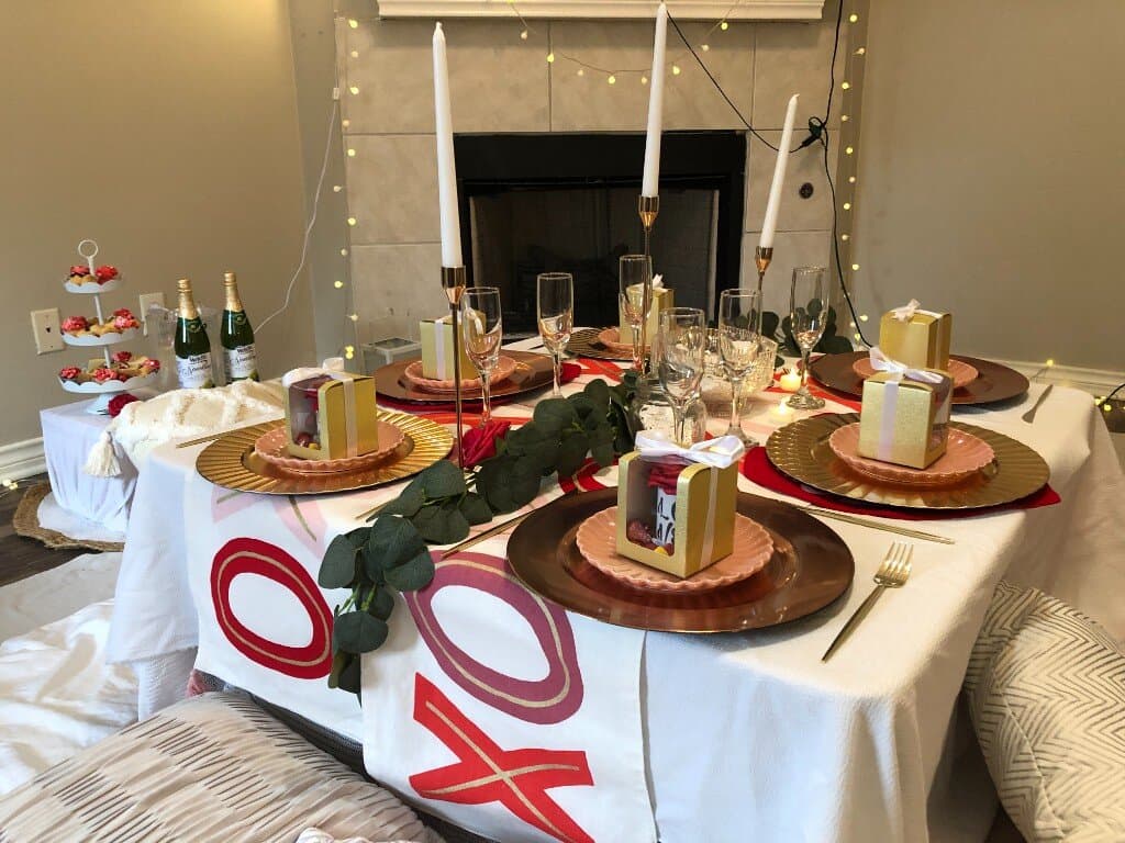 Indoor Valentine’s picnic setup with rose-gold chargers, gifts, and string lights