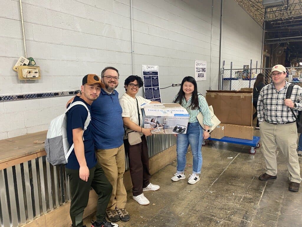 Team in the BIDFTA.com Testing Area holding a product box on the warehouse floor