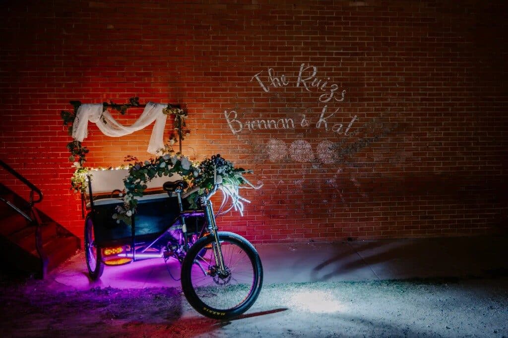 Decorated wedding pedicab with The Ruizs monogram projected on a brick wall
